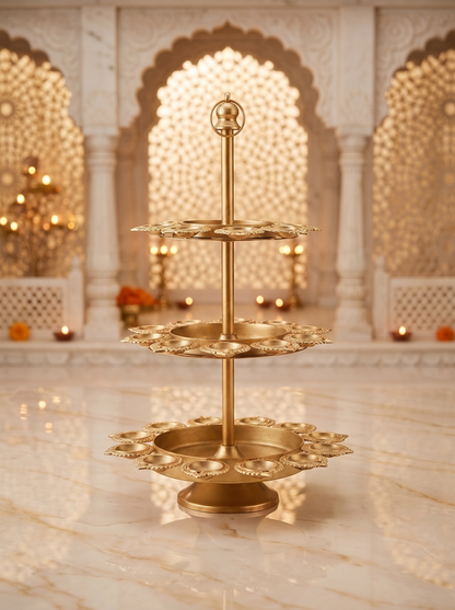 Gold 3-tier lotus diya stand with kalash finial, front view in a festive mandir setting