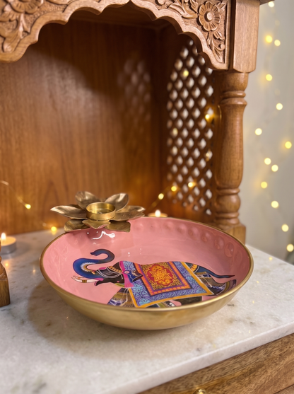Pink enamel urli bowl with elephant print, gold rim and lotus tealight centre, front view in a festive setting