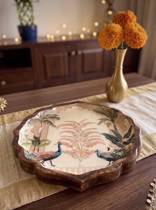 Scalloped round wooden platter with peacock and palm garden print, front view in a festive setting