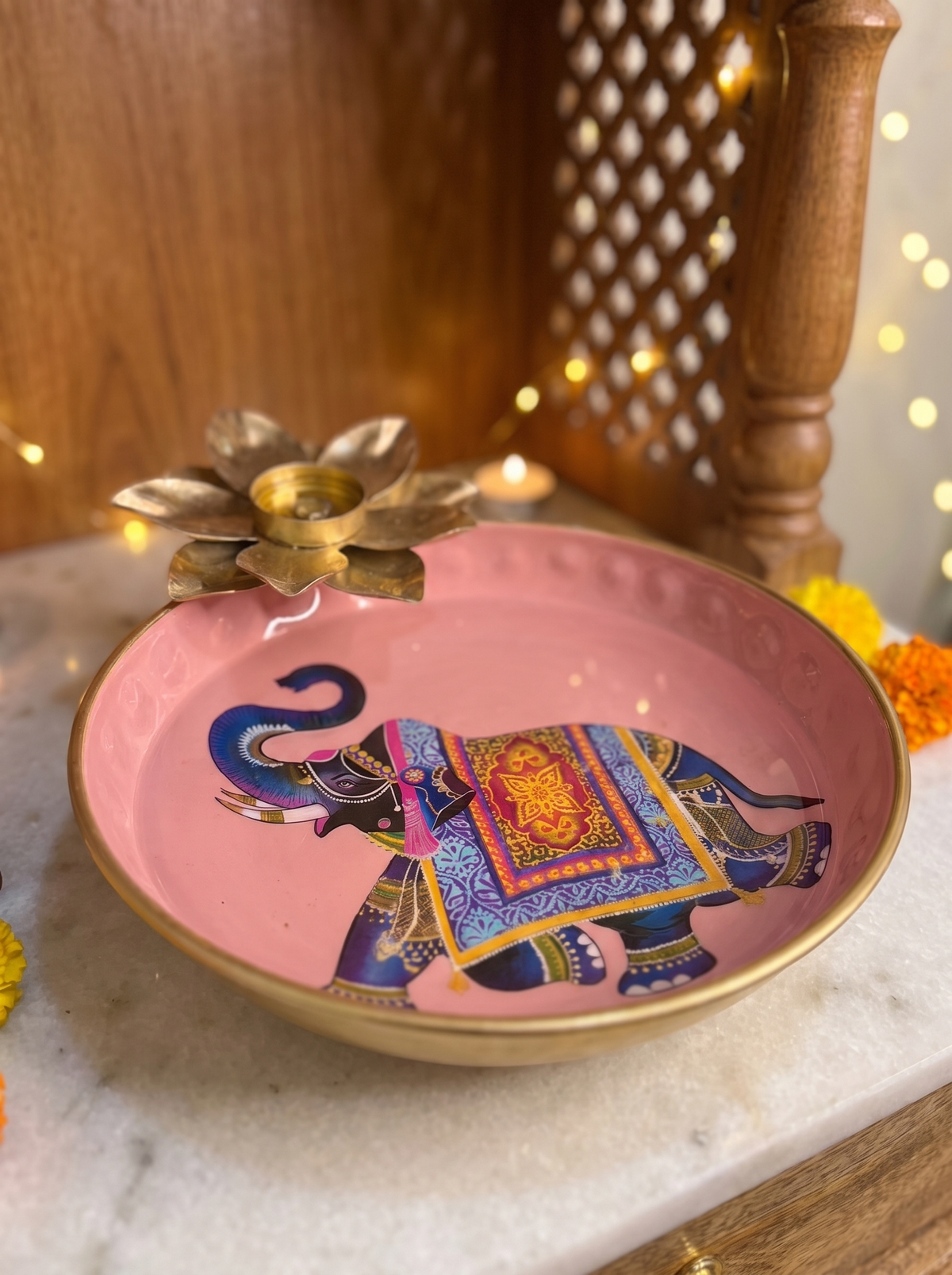 Close-up detail of elephant print and gold lotus tealight holder on pink enamel urli