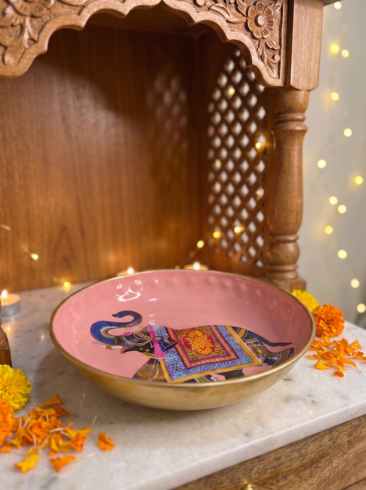 Pink elephant print urli bowl with lotus tealight, angled view with marigolds