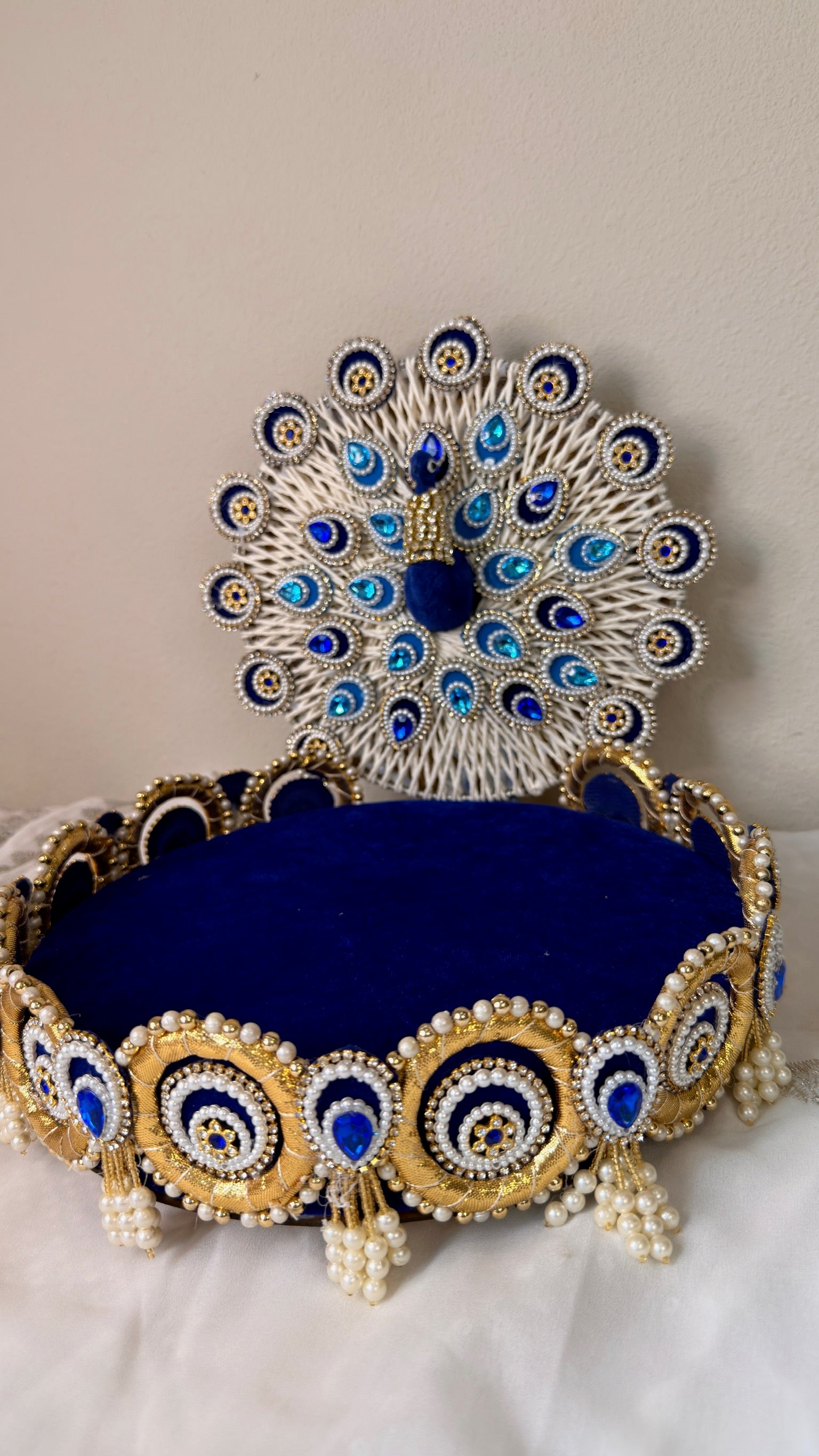 Royal blue peacock singhasan showing pearl tassels and gold trim, Krishna idol seat