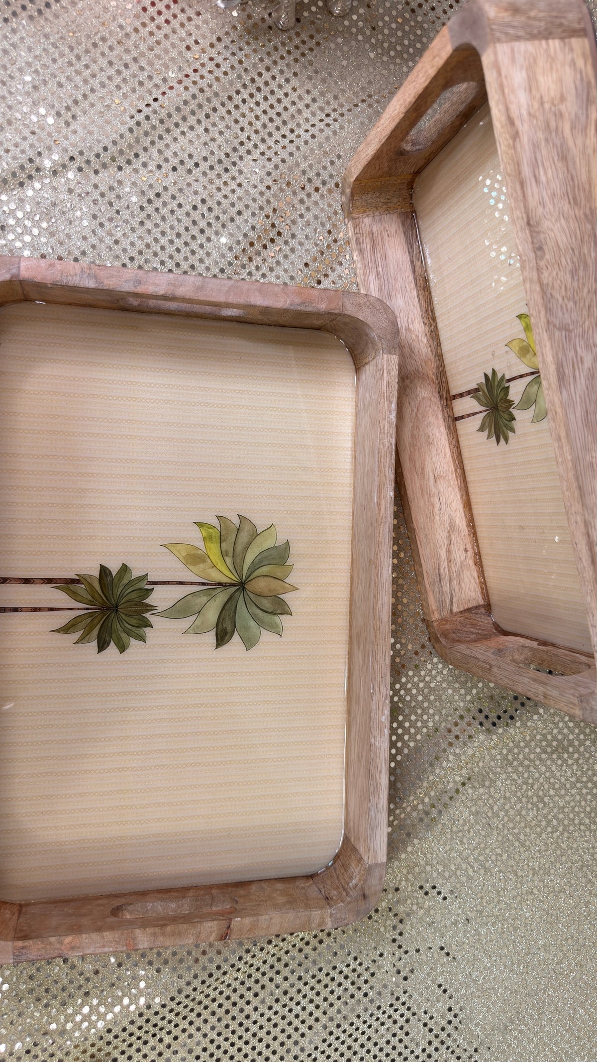 Two palm print mango wood trays laid side by side on sequin cloth