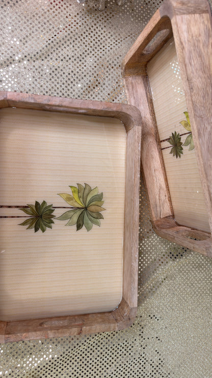 Two palm print mango wood trays laid side by side on sequin cloth